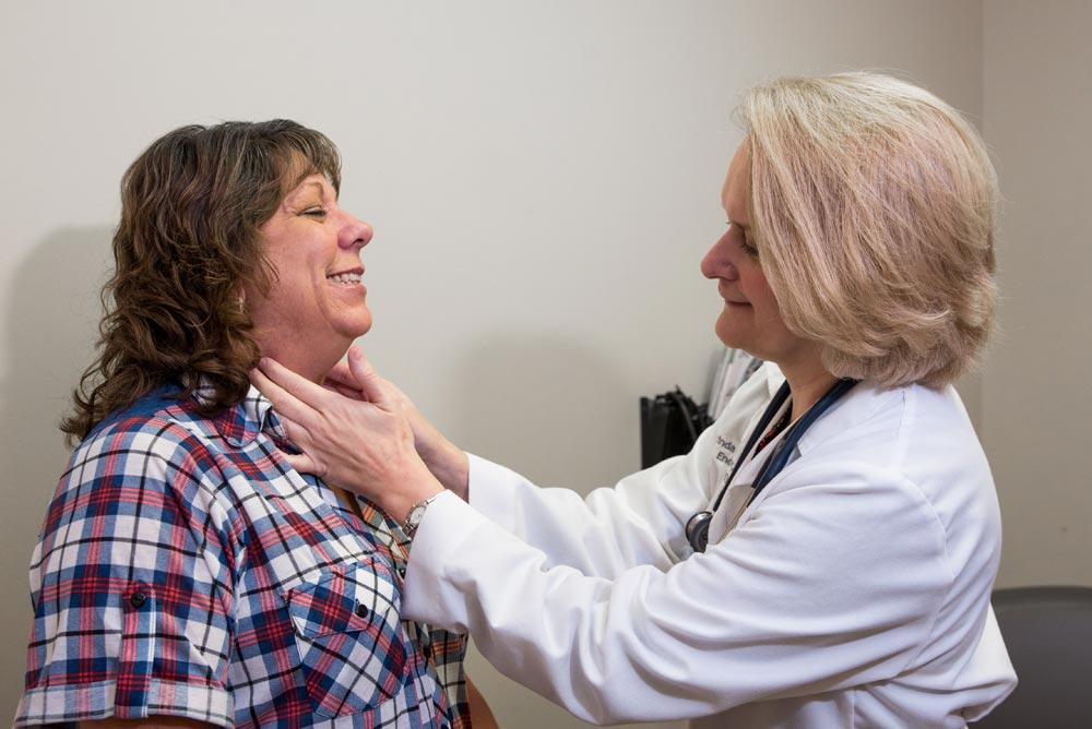 A primary care doctor in white coat checking patient's neck