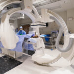Patient undergoing biplane angiography in a hospital interventional radiology suite with Siemens imaging equipment.