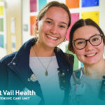 Two pediatric ICU nurses smiling together in a hallway, wearing badges, with Stormont Vail Health logo.