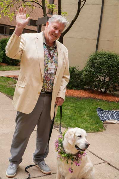 Person waving while standing with golden retriever therapy dog