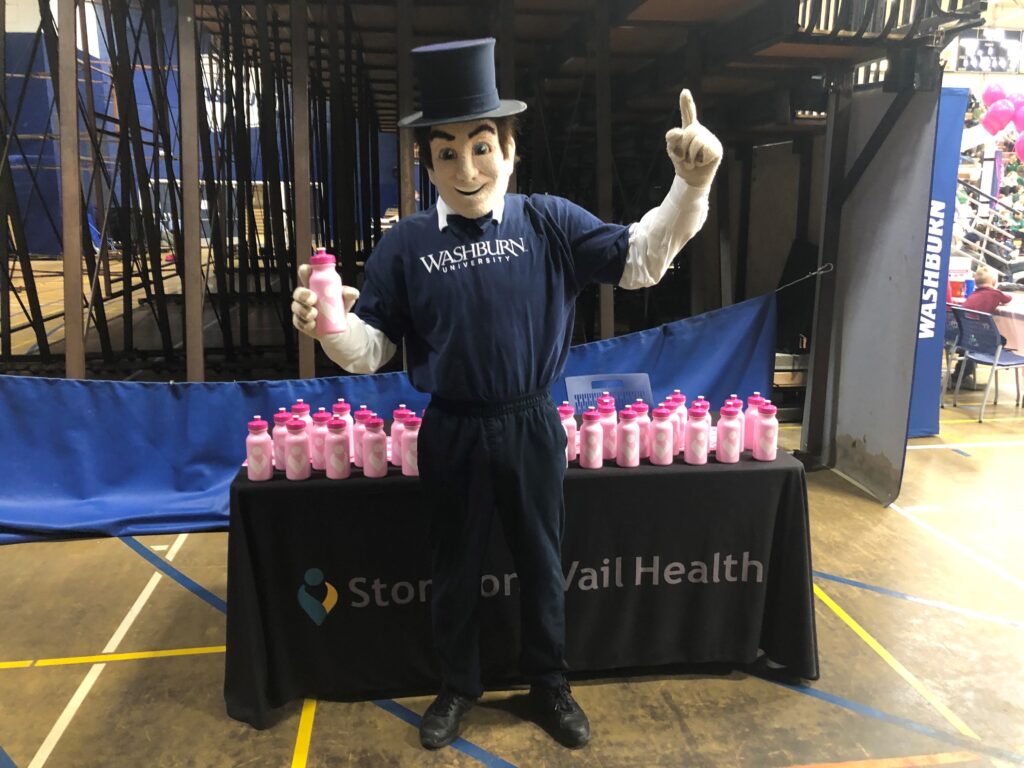 Washburn University Ichabod posing with the pink water bottles that have Stormont Vail Health logo on them.
