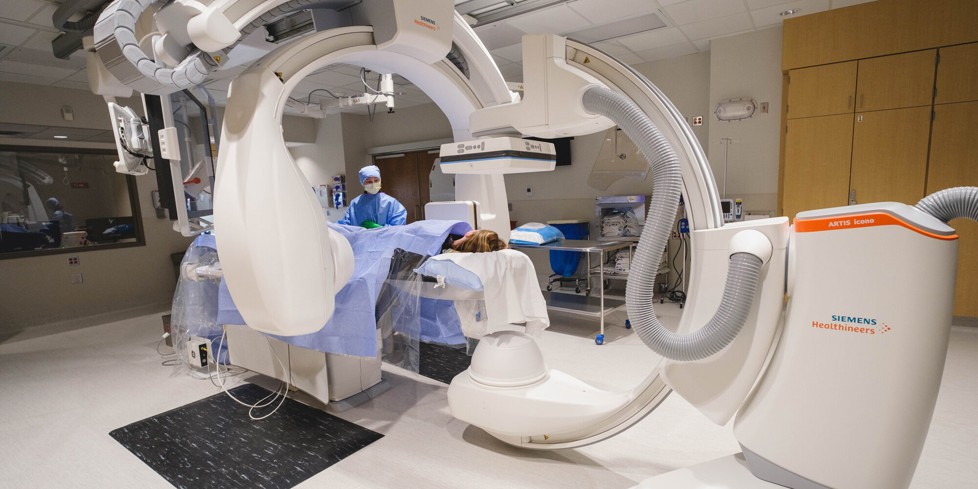 Patient undergoing biplane angiography in a hospital interventional radiology suite with Siemens imaging equipment.