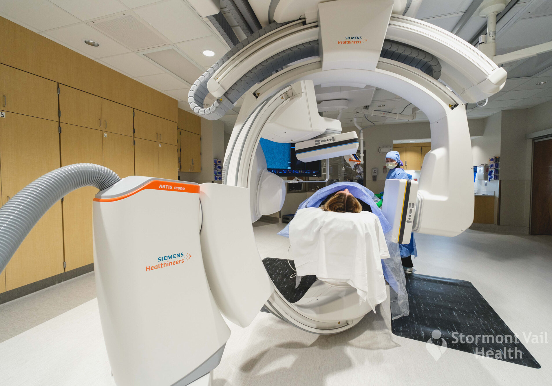 Patient undergoing biplane angiography in a hospital interventional radiology suite with Siemens imaging equipment.