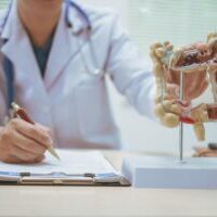 Clinician pointing to a model of the colon while writing on a clipboard, highlighting patient education about digestive health.