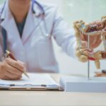 Clinician pointing to a model of the colon while writing on a clipboard, highlighting patient education about digestive health.